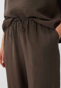 Pantalons en tissu léger marron avec une taille élastique et un cordon de serrage. Comprend deux poches latérales et une coupe décontractée pour le confort.