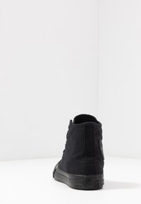 Svart lerret høyhælte sneakers med gummisåle, snørehull, rund tå og et sirkulært logo-patch på baksiden.