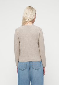 Beige knitted sweater with long sleeves, round neckline, and a smooth texture. Paired with high-waisted blue denim jeans.