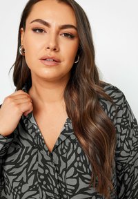 Black and gray patterned blouse with a collar, buttoned front, and two chest pockets, paired with large silver hoop earrings.