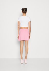 Bílý krátký tričko v kombinaci s růžovou mini sukní ve tvaru A. Modelka má na sobě světle růžové boty na blokovém podpatku, které mají hladký povrch a jednoduchý design.