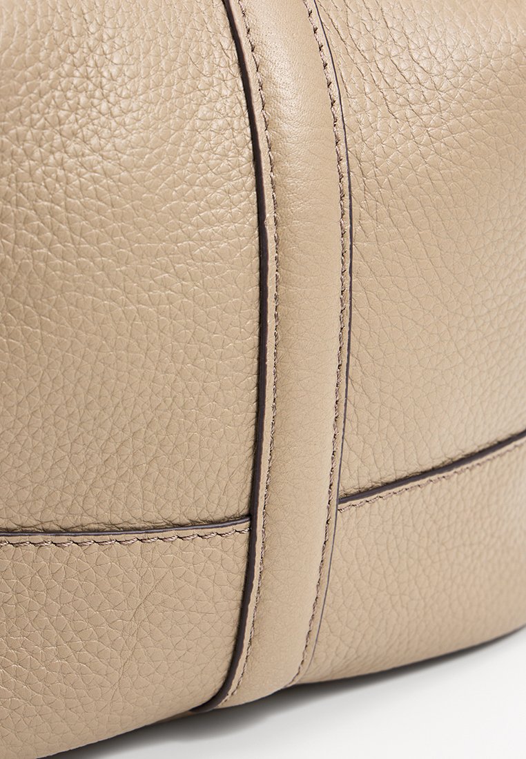 Beige leren handtas met een textuur oppervlak, opvallende stiksels en een verhoogde naaddetail. Rond gevormd met minimale accenten.