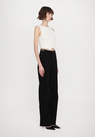 White, sleeveless crop top with a curved hem; paired with high-waisted, black wide-leg trousers featuring golden accents and pockets.