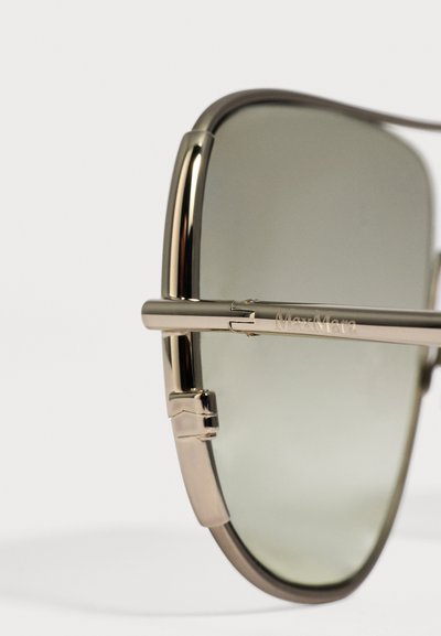 Gros plan de lunettes de soleil à monture métallique dorée avec des verres teintés gris et "MaxMara" gravé sur la branche fine.