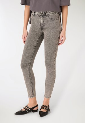 Persona che indossa jeans skinny a vita alta effetto acid wash abbinati a ballerine slingback nere con punta appuntita e cinturini con fibbia.