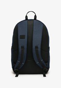 Sac à dos bleu marine avec dos en mesh noir rembourré et bretelles ajustables. Il présente un tissu texturé et une petite étiquette noire à l'avant.