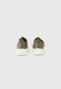 Sneakers in tessuto verde con suole bianche, caratterizzati da una parte superiore testurizzata e un cinturino sul retro, progettati per comfort e traspirabilità.