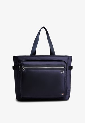 Granatowa torba na ramię z dwoma uchwytami, przednią kieszenią na zamek, detalami z klamrami po bokach oraz małym prostokątnym logo w dolnym prawym rogu.