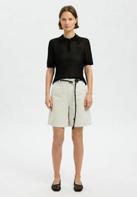 Svart randig kortärmad pikétröja i kombination med ljusbeige knälånga shorts med flätad bälte och texturerade svarta skor.