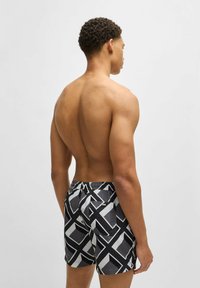 Shorts de bain noirs et blancs à motifs avec taille à cordon et poche arrière, présentant des formes géométriques et une texture lisse.