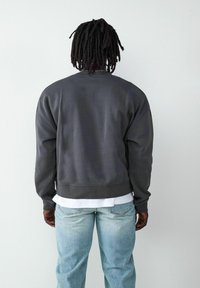 Szara bluza z luźnym krojem i ściągaczem na dole, zestawiona z jasnoniebieskimi dżinsami. Posiada długie rękawy i prosty design.