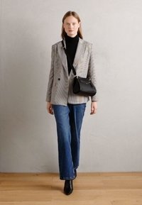 Blazer con motivo a quadri in scala di grigi, indossato sopra un dolcevita nero, abbinato a jeans a zampa d'elefante blu e stivaletti neri, con una borsa nera.