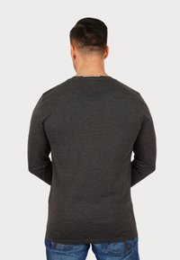 Long-sleeve dark grey shirt, crew neck design, soft texture, plain back with a small colored label at the neck. Worn with blue jeans.
