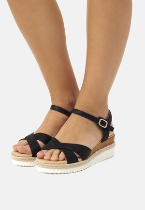 Sorte sandaler i ruskind med justerbar ankelrem, krydsremme og kilehæl med naturlig juteaccents og hvid gummibund.