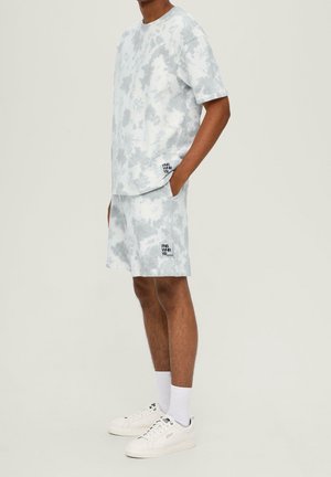 Lysegråt tie-dye t-shirt og shorts sæt, lavet af et blødt stof, med sorte logoaccenter nederst til venstre på begge dele.