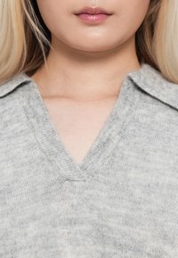 Maglione grigio a scollo a v con un morbido tessuto a maglia testurizzata e un design con colletto, che mostra una leggera variazione di colore e una finitura liscia.