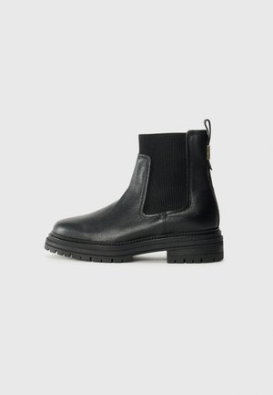 Stivale alla caviglia in pelle nera con pannelli laterali elasticizzati a coste e linguetta di pull. Sole in gomma spessa e texture con un modello di battistrada definito.