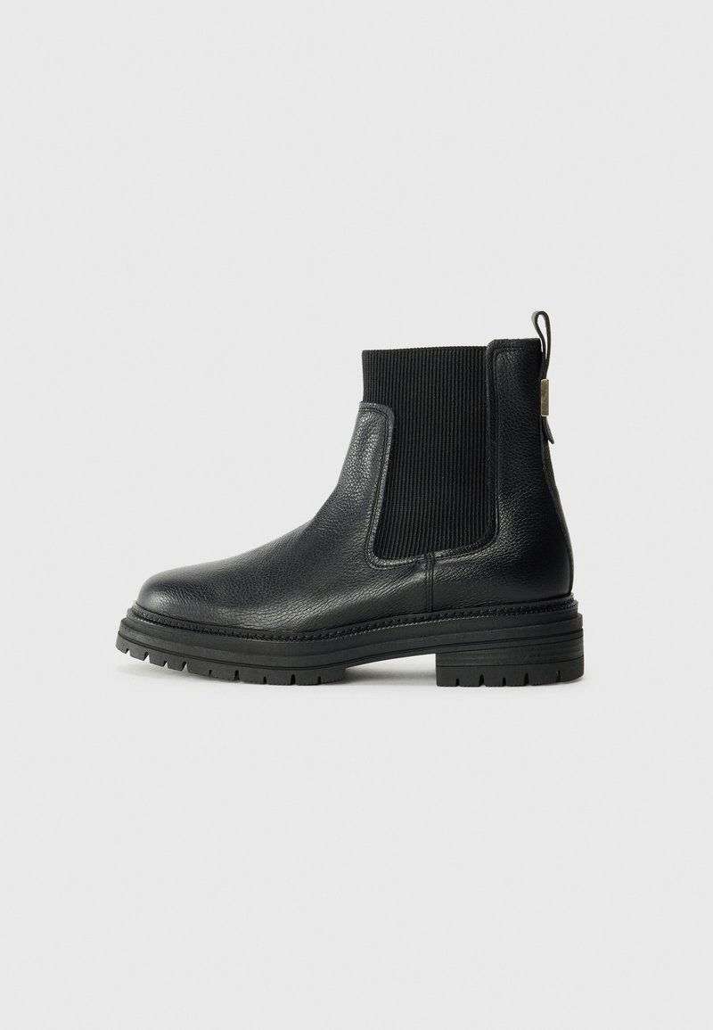 Stivale alla caviglia in pelle nera con pannelli laterali elasticizzati a coste e linguetta di pull. Sole in gomma spessa e texture con un modello di battistrada definito.