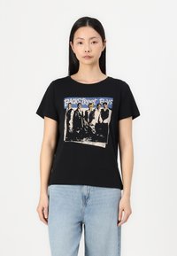 T-shirt noir avec un col rond, featuring un graphisme imprimé de six figures en costume et le texte "Backstreet Boys" en bleu au-dessus. Matériau en coton.