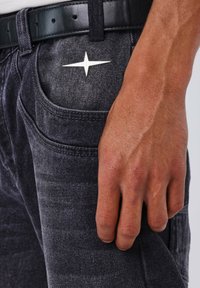 I jeans in denim scuro presentano un tessuto textured con una stella argentata accentata sulla tasca anteriore, completati da una cintura nera.
