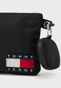 Mustasta nailonista valmistettu vetoketjullinen pussi, jossa sininen, valkoinen ja punainen kirjailtu logo. Sisältää pienen, kiinnitetyn pussukan.