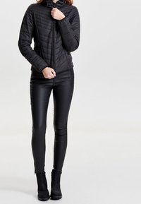 Czarna ocieplana kurtka z zapięciem na zamek i kapturem. Połączona z dopasowanymi czarnymi spodniami z ekoskóry i botkami do kostki. Gładka tekstura; elegancki design.