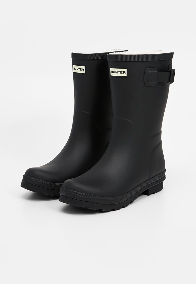Schwarze Gummiregenstiefel mit glatter Oberfläche, strukturierten Sohlen und einem Schnallenverschluss an der Seite. Mit einem weißen Markenlabel an der Vorderseite.