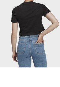 Svart kortärmad t-shirt med croppad design. Bärs med ljusblå högmidjade jeans med bakfickor och en urblekt textur.