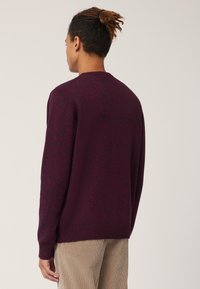 Maglione a maglia bordeaux con polsini e orlo a costine, caratterizzato da un motivo texture. Modello mostrato di spalle, abbinato a pantaloni in velluto a coste.