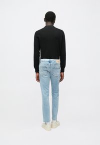 Μαύρο πλεκτό πουλόβερ, ανοιχτό μπλε τζιν παντελόνι με στενή γραμμή και πίσω τσέπες, και λευκά αθλητικά παπούτσια, φωτογραφημένα από πίσω μπροστά σε απλό λευκό φόντο.