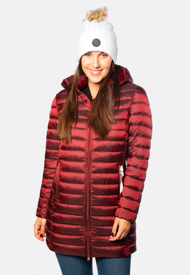 Doudoune rouge avec un matelassage horizontal, un col haut et une fermeture éclair à l'avant. Associée à un bonnet en tricot blanc avec un pompon en fausse fourrure.