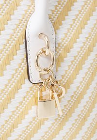 Sac en paille tressée avec des accents en cuir blanc, affichant un verrou doré et un porte-clés détaillé. Motif texturé jaune et blanc.