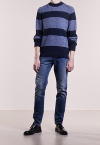 Marinblå och ljusblå randig tröja med strukturerad stickning, rundad halsringning och långa ärmar, tillsammans med blå jeans och svarta finskor.