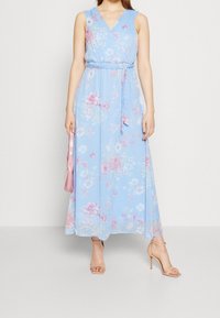 Blommig maxiklänning i ljusblått, med V-ringning, ärmlös design och bälte i midjan. Fina rosa och vita blommönster överallt.