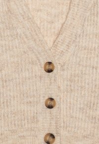 Beige stickad cardigan med V-ringning, som har fem runda bruna knappar och en ribbad struktur för extra detalj.