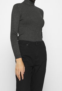 Jersey de cuello alto acanalado gris con mangas largas, combinado con pantalones vaqueros negros de talle alto. Textura suave con diseño ajustado.