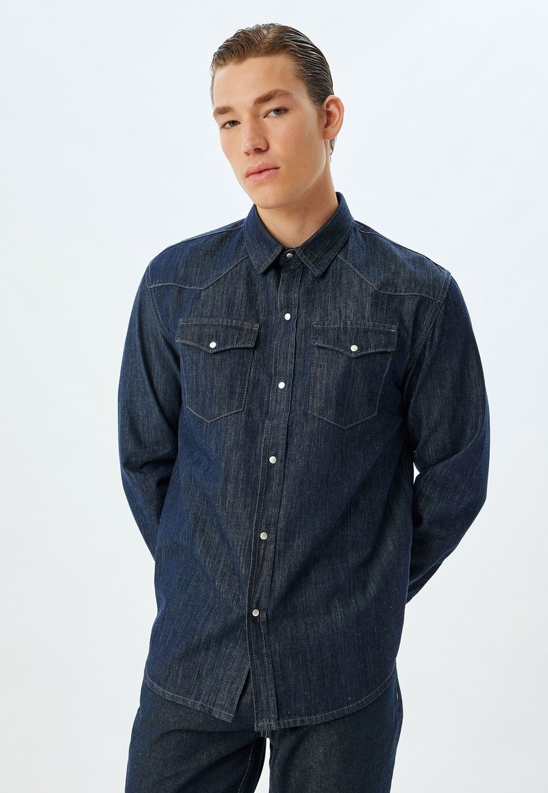 Jeansskjorta i mörkblått med knapplist, två bröstfickor och kontrasterande sömmar. Har långt ärm och en avslappnad passform.