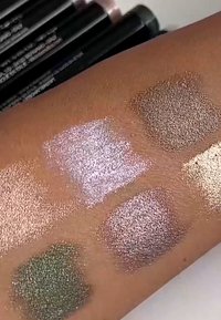 Prøver av skinnende øyenskygge på hud: pastellrosa, dempet grønn, lys beige, varm bronse og iriserende taupe, som viser ulike finish.