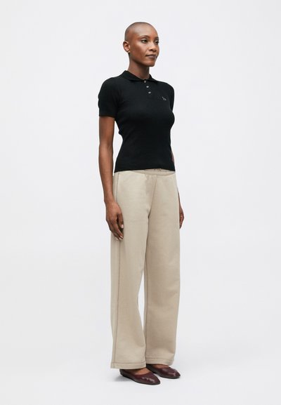 Melna ribota polo krekls ar īsām piedurknēm, apvienots ar brīviem bēšiem biksēm un tumšiem plakanajiem apaviem. Vienkāršs dizains, nav redzamu rakstu vai rotājumu.