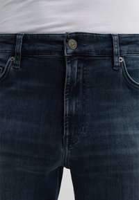 Dunkelblaue Denim-Jeans im klassischen Fünf-Taschen-Design, ausgestattet mit einem Knopfverschluss, Gürtelschlaufen und dezenten Ausbleichungen für eine interessante Textur.