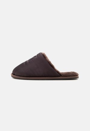 Zapatilla sin cordones de color marrón oscuro con interior suave y aterciopelado y suela plana, mostrada de lado sobre un fondo claro y liso.