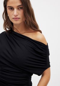 Musthave musta off-shoulder kleit kogutud tekstuuriga. Pehme, veniv kangas ja figureeriv siluett. Ühe rihmaga disain.
