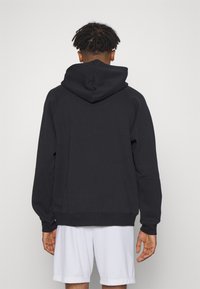 Hoodie noir avec une capuche de taille moyenne, des poignets côtelés et une texture lisse, conçu avec une coupe décontractée et un design minimaliste.