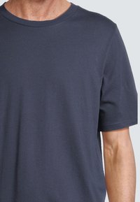 T-shirt à manches courtes bleu marine, en tissu lisse, avec un col rond et une coupe décontractée. Pas de motifs ni d'accents visibles.