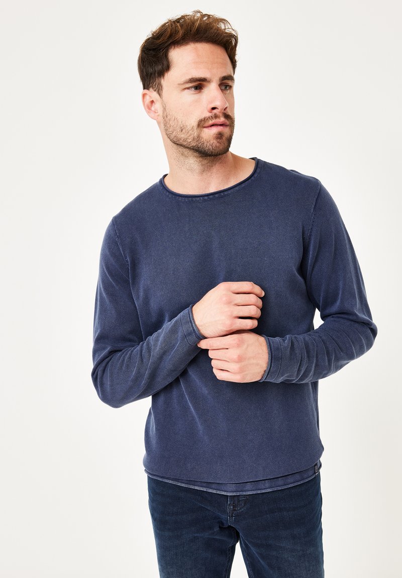 Marineblaues Langarmshirt mit Rundhalsausschnitt aus strukturiertem Stoff, mit gesteppten Akzenten und schmalen Bündchen. Kombiniert mit dunklen Jeans.