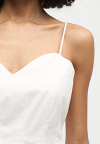 Κοντινό πλάνο μιας γυναίκας που φοράει λευκό αμάνικο τοπ με λεπτές τιράντες σπαγγέτι και ντεκολτέ σε σχήμα καρδιάς.