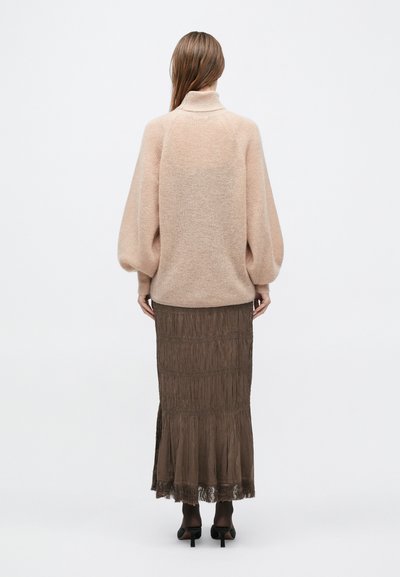 Bézs kötött pulóver magas nyakrésszel és puffos ujjakkal, barna, réteges, rojtos maxiszoknyával párosítva. Mindkét darab puha tapintású.