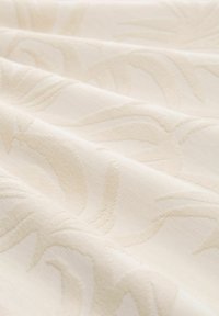 Krämfärgad tyg med texturerade, präglade blommönster. Slät och mjuk yta med en subtil lyster, som faller elegant.