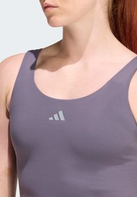 Lila Sporttanktop mit glatter Textur und breiten Trägern. Verfügt über ein kleines, hellgraues Logo mit drei Streifen im Brustbereich.
