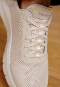 Bež Skechers GOwalk tenisice s mrežastim gornjim dijelom, ravnim vezicama i mekanim potplatom. Vidljivi brend na peti. Teksturirana površina za prozračnost.